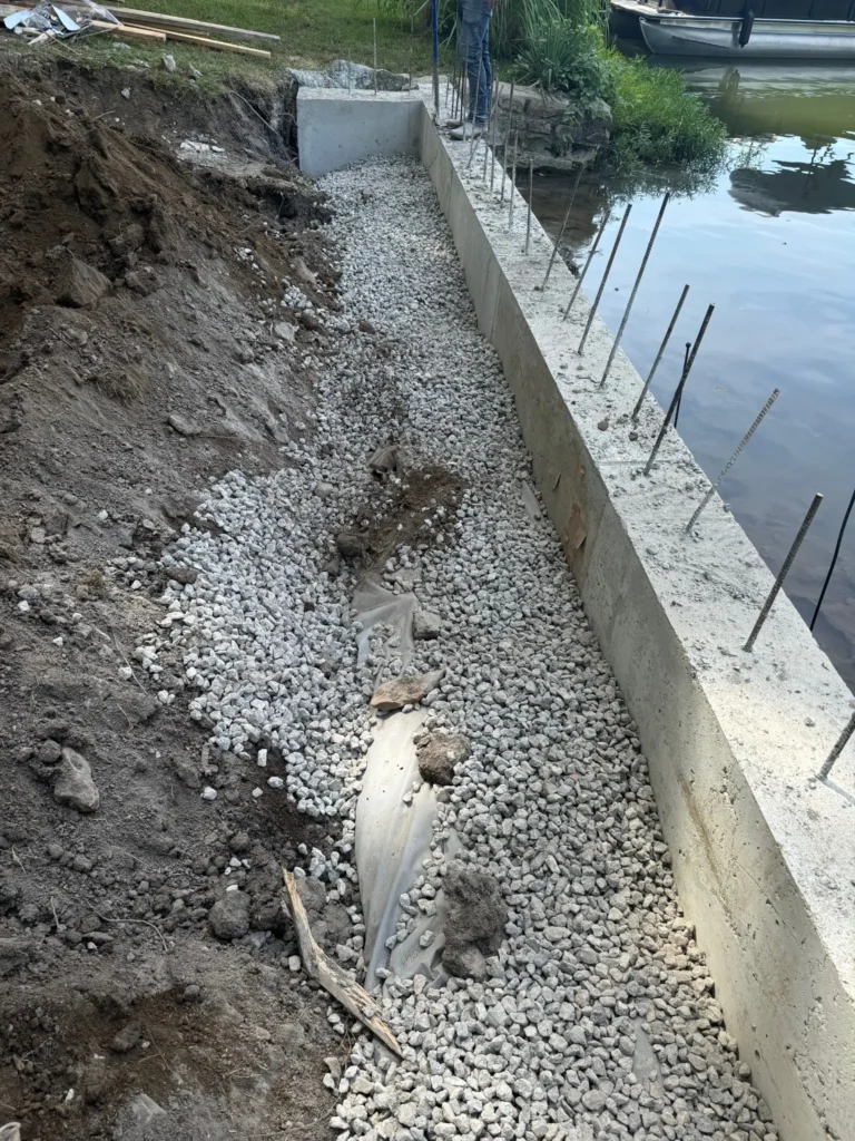 Gravel drainage backfill installed behind a concrete seawall along a residential shoreline in Kansas City