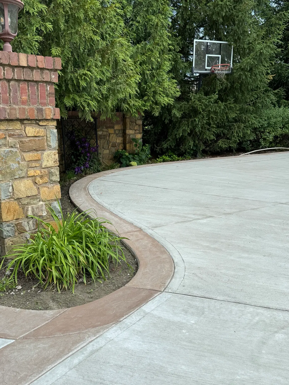 Finished concrete driveway with curved decorative border around residential landscaping