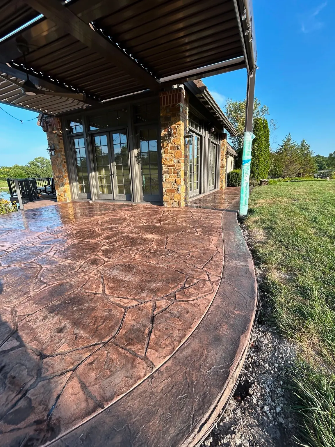 Large brown stamped concrete patio beneath a pergola beside a boathouse.