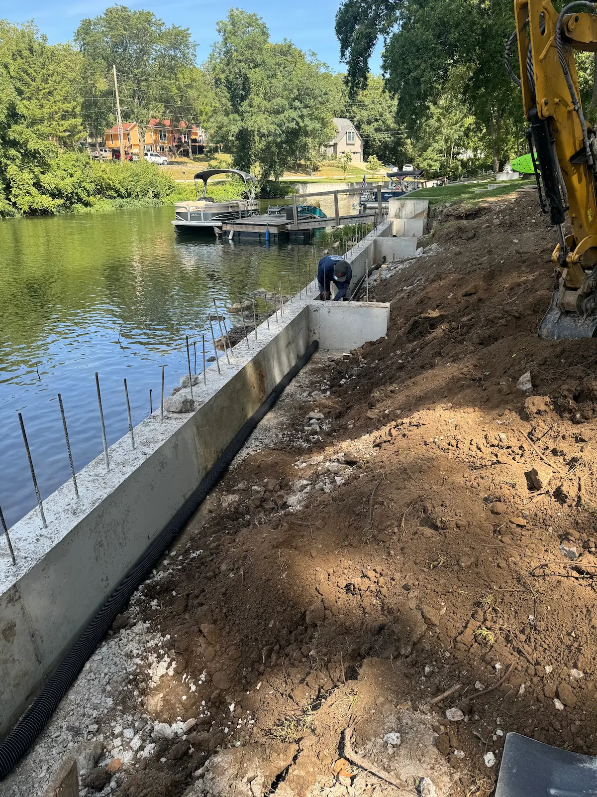 Concrete seawall under construction in Kansas City with reinforcement, drainage pipe, excavation, and shoreline access